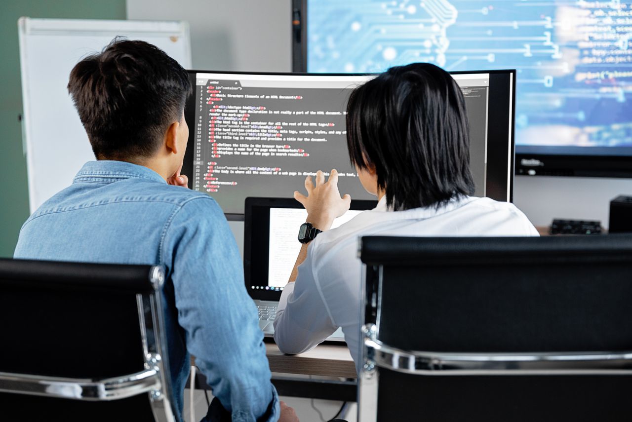 services-01 Two developers working together in an office, discussing code on a screen. Technology teamwork setting.