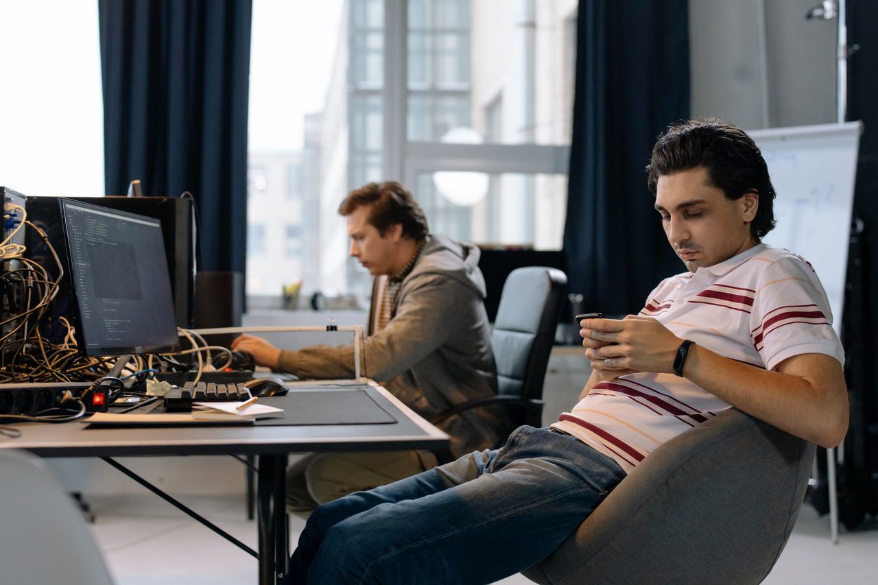 The Art of Drawing Readers In: Your attractive post title goes here Two men working in a modern office, one on a computer and the other on a smartphone.